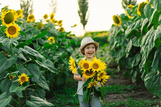 ひまわり畑を歩く幸せな男の子大きな花で遊んで楽しんでいる子