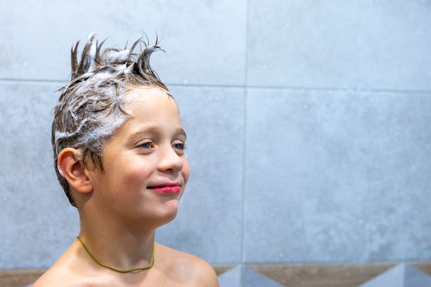 A happy boy washes his head in the bathroom with shampoo