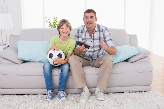 Partita di calcio di sorveglianza del ragazzo felice con il padre sul sofà