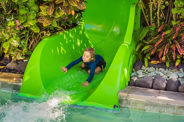 Foto ragazzo felice sullo scivolo d'acqua in una piscina che si diverte durante le vacanze estive in un bellissimo resort tropicale