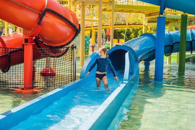 Happy boy on water slide in a swimming pool having fun during summer vacation in a beautiful tropical resort