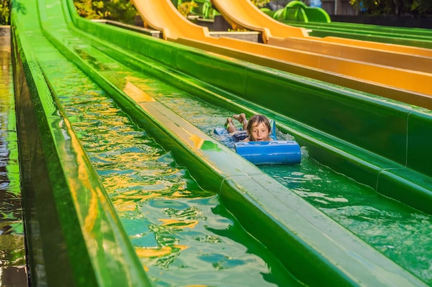 Happy boy on water slide in a swimming pool having fun during summer vacation in a beautiful