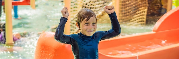 Happy boy on water slide in a swimming pool having fun during summer vacation in a beautiful