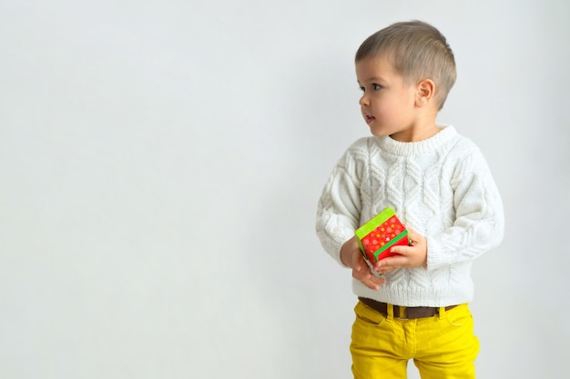 A happy boy in a white sweater and yellow jeans holding gift box