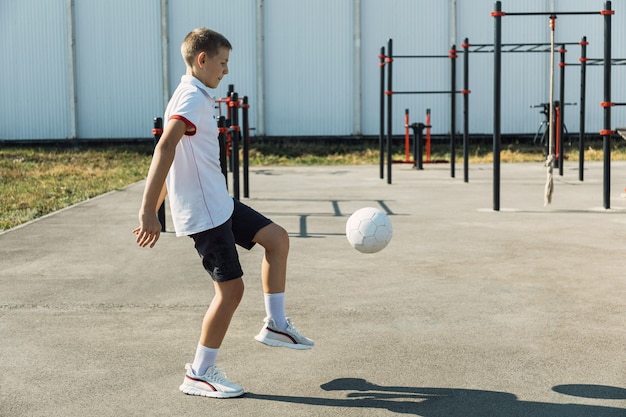 Happy boy in white t shirt working out on the sports ground ball exercises.