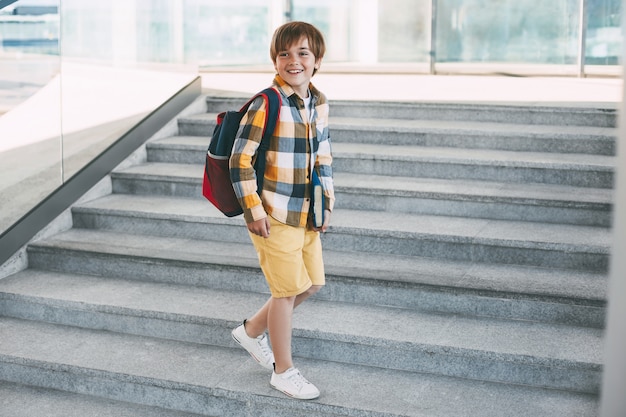 バックパックと本を持って幸せな少年は学校に行く