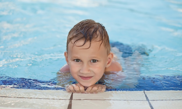 Happy boy with blond hair smiling sitting in swimming pool