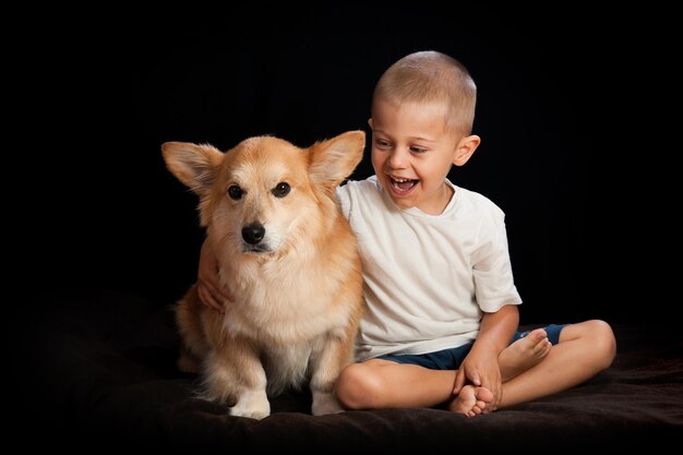 ダークルームでベッドに座っている犬を持つ幸せな少年