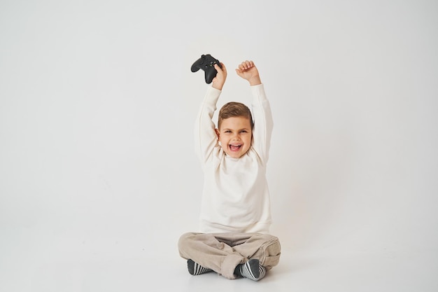 Счастливый мальчик с геймпадом поднимает руки вверх и кричит Эмоциональный ребенок выиграл консольную игру