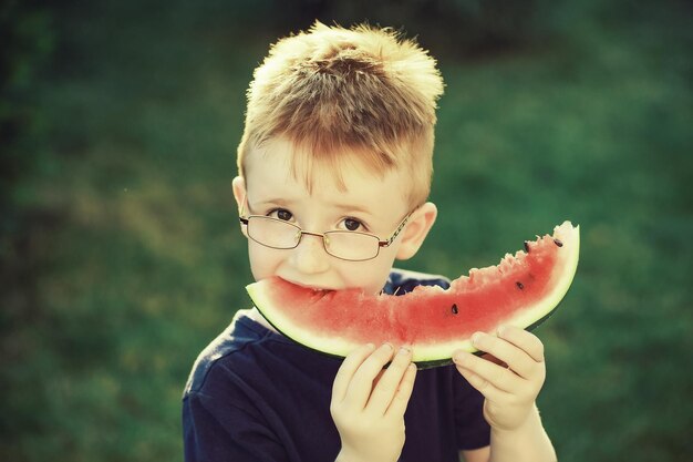 Happy boy with red hair in glasses eating watermelon