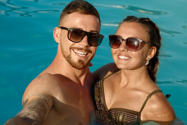 Happy boyfriend and girlfriend taking selfie while resting in the swimming pool