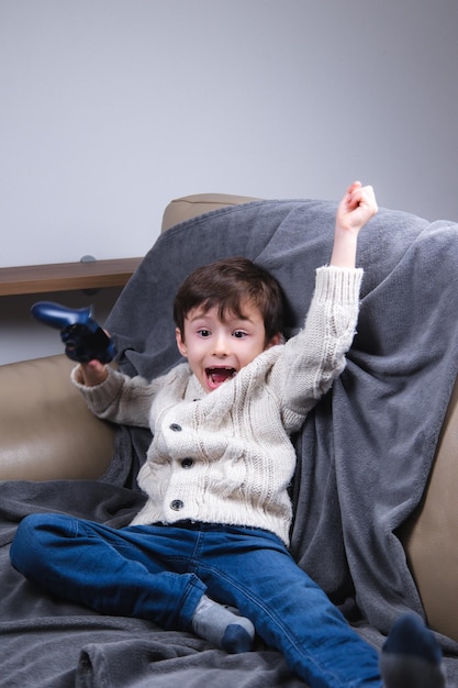 Happy boysiting op de bank houdt een game-joystick vast en verheugt zich over de overwinning in de videogame