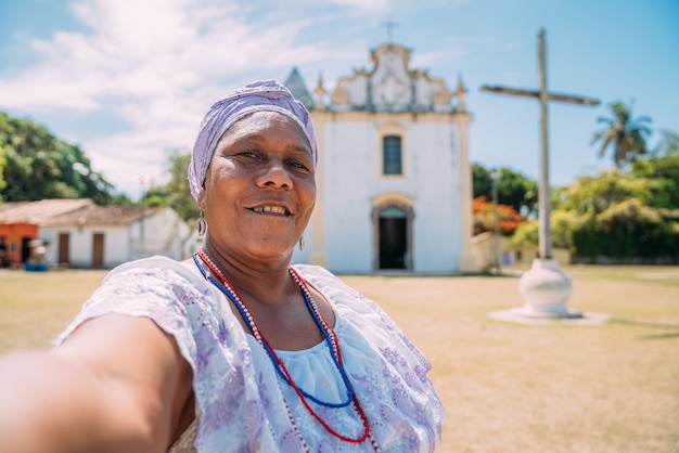 Happy Brazilian woman of African descent dressed in the traditional Bahian dress making a selfie in front of the church