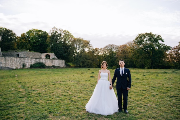 Happy bride and groom are standing on green grass and holding hands Love concept