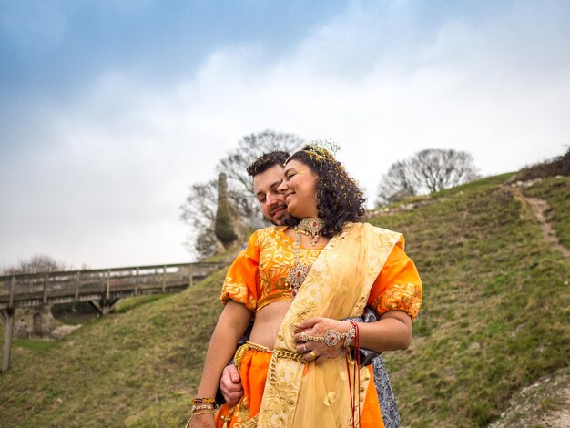 Foto una sposa e uno sposo felici che fanno l'amore sul campo contro il cielo.