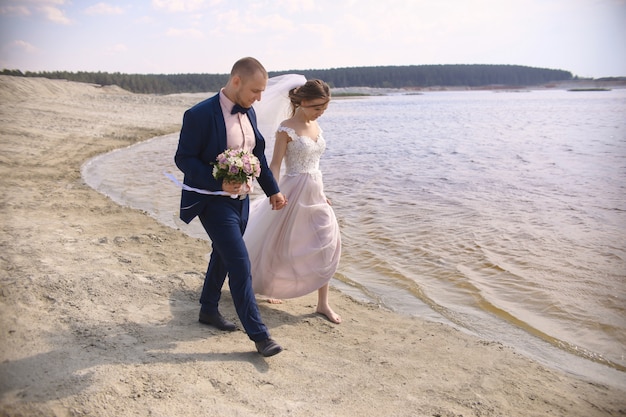 Happy bride and groom run along the shore lake