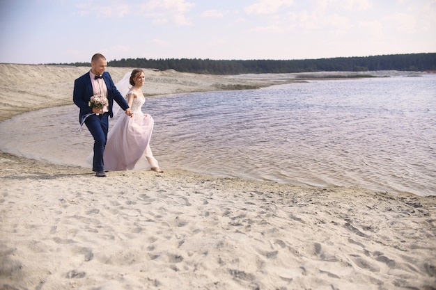 Happy bride and groom run along the shore lake