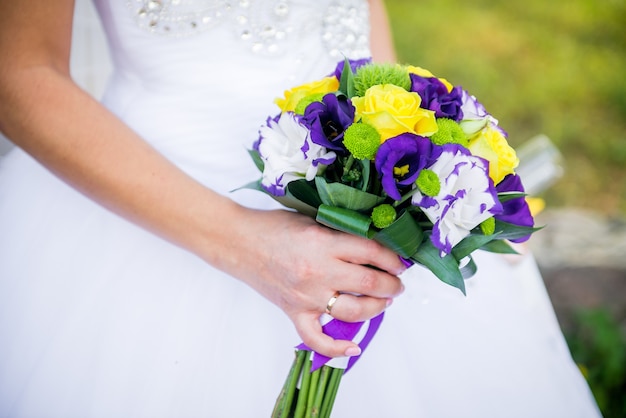 Happy bride holds a wedding bouquet in hands. Wedding bouquet of purple, yellow and white flowers in their hands and a young bride.