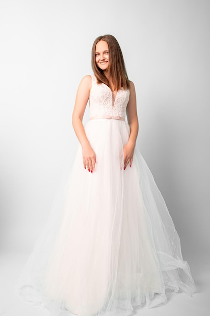 Happy bride. Special wedding day. Festive shooting. Smiling women in white fluffy dress posing on camera in studio isolated on light.