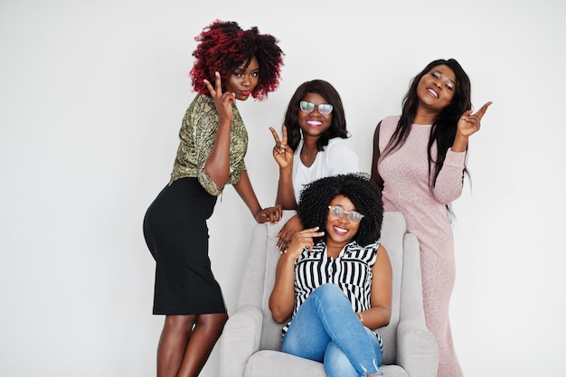 Happy brightful positive moments of four african girls Having fun and smiling on chair against white empty wall Lovely moments of four best friends Show two viva fingers