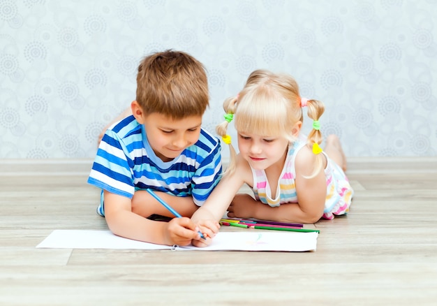 Happy brother and sister draw while lying on the living room floor. Children draw with pencils at home.