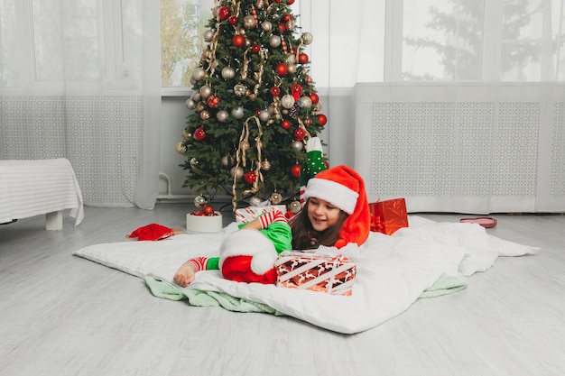 Happy brother and sister dressed as Santa Claus are sitting near the Christmas tree at home in the living room with gifts. Christmas