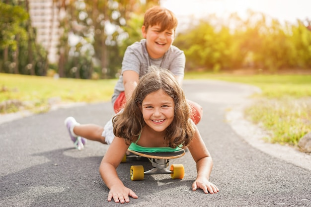 Happy brother and sister playing with longboard outdoor - Young people having fun in summer time outside