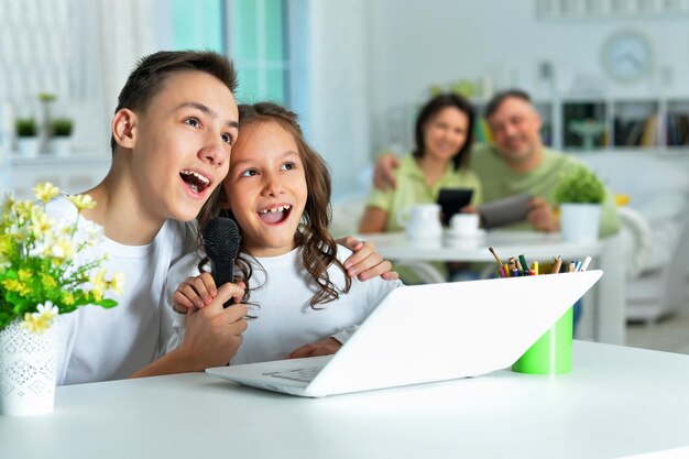 Photo happy brother and sister using modern laptop and singing