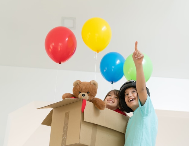 Счастливые братья, играющие с воздушными шарами и картонной коробкой