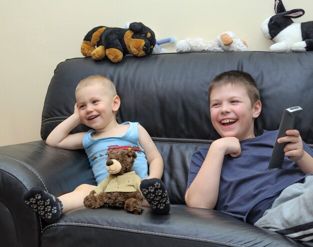 Happy brothers watching TV on leather couch and having fun together.