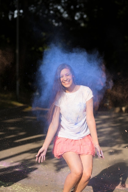 Photo happy brunette asian woman jumping with holi paint exploding around her