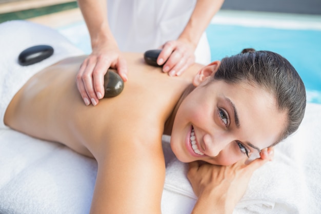 Happy brunette getting a hot stone massage poolside