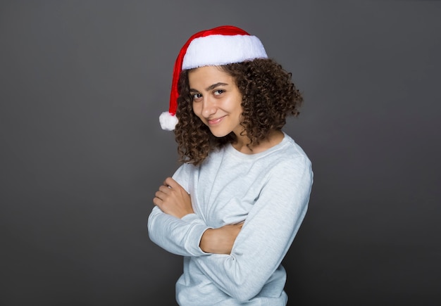 Happy brunette girl in Santa Claus Christmas hat on black . 