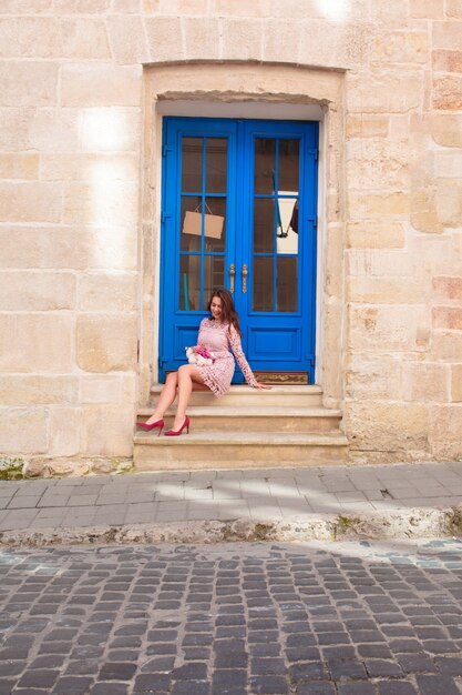 Happy brunette model in trendy lace dress holding bouquet of flowers. woman sitting at the door