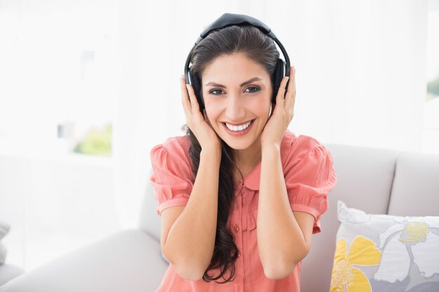 音楽を聞く彼女のソファーに座っている幸せなブルネット