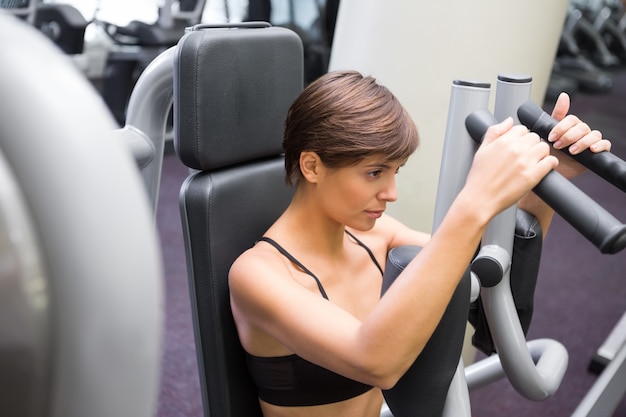 Happy brunette using weights machine for arms