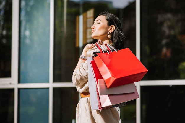 Happy brunette woman holding shopping bags outdoors. Shopoholic woman satisfied with the purchases