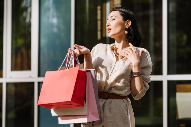 屋外で買い物袋を保持している幸せなブルネットの女性。買い物に満足している買い物好きの女性