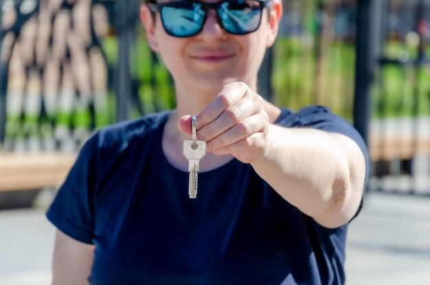 Happy brunette woman holds the keys to a new apartment against the background of new buildings