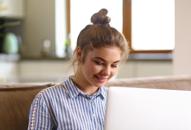 Happy brunette woman sitting on sofa with laptop