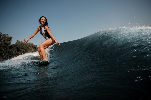 Donna felice del brunette che pratica il surfing a bordo giù l'acqua blu