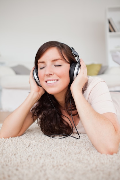 Happy brunette woman using headphones while lying on a carpet