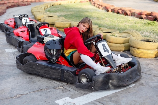 カートトラックで夏にポーズをとって赤いスポーツスーツでカートレースoungブロンドの女の子に勝つ幸せなブルネットの女性