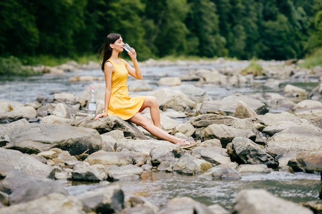 Happy brunette in yellow dress sitting on stones