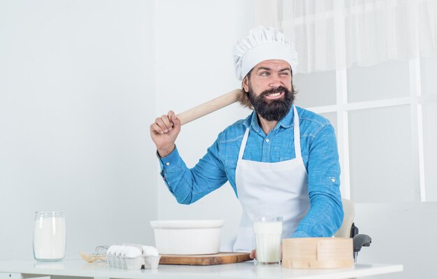 Happy brutal hipster with moustache and beard in apron cooking meal, culinary.