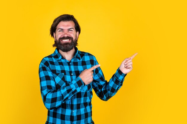 Happy brutal man in checkered shirt has long beard pointing finger copy space ad