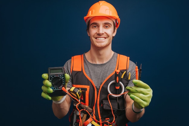 Happy builder is holding digital multimetert in gloves