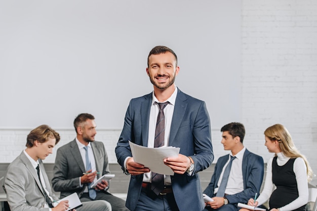 Happy business coach standing in front of businesspeople at training in hub