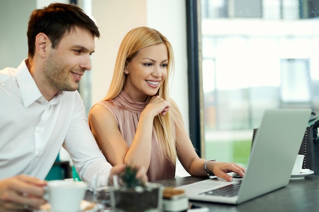 Happy business couple surfing the net on a computer while sitting in a cafe