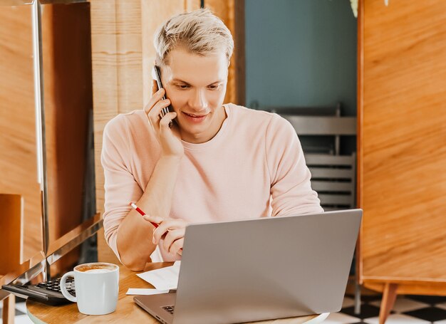 Happy business man sitting at cafeteria with laptop and smartphone. Businessman texting on smart phone while sitting in a cafe, working and checking email on computer